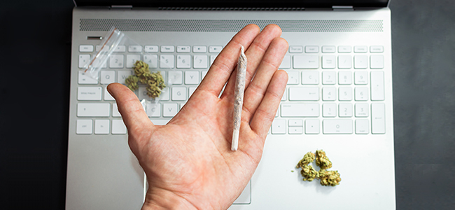Top view of hand holding a big marijuana joint with computer and